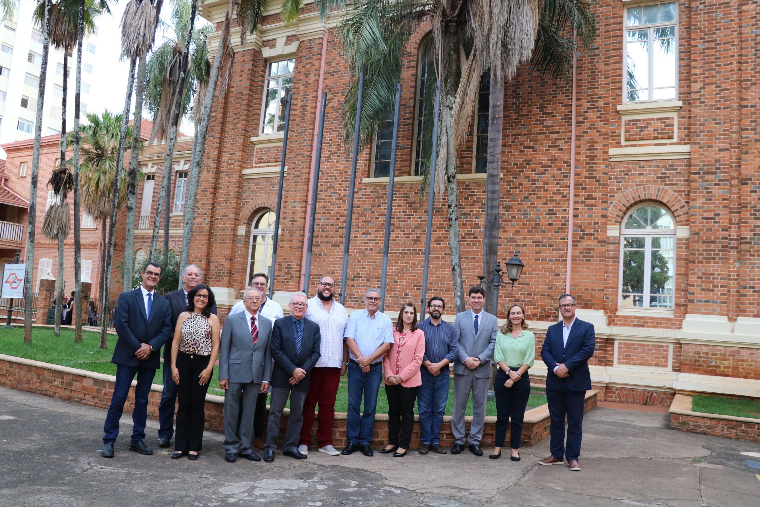 Na foto aparecem os representantes do CRMV-SP e da Unimep. Estão todos de pé, posam e sorriem para a câmera, e estão posicionados em frente a uma construção história com tijolos de barro aparentes cercada por uma jardim com palmeiras. São 10 homens e três mulheres no total.