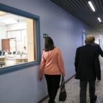 Na foto aparece a tesoureira e o presidente do CRMV-SP de costas em um corredor de salas de aula da Unimep. Na parede a esquerda há uma grande janela de vidro em que é possível observar um dos laboratórios da instituição.
