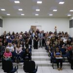 Mais de 120 estudantes da graduação em Medicina Veterinária da Unesp estão sentados nas cadeiras do auditório do Hospital Veterinário. No corredor central estão de pé o presidente, o vice-presidente e a tesoureira do CRMV-SP, acompanhados da representante regional da autarquia em Araçatuba e do representante da Feveresp. Todos posam e sorriem para a foto.