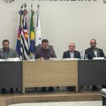 Na imagem aparece o plenário da Câmara Municipal de Sebastianópolis do Sul. O presidente do CRMV-SP compõe a mesa ao lado dos vereadores e o presidente da Casa Legislativa. Atrás deles estão as bandeiras do país, do estado e do município. E eles estão sentados atrás das mesas do plenário.