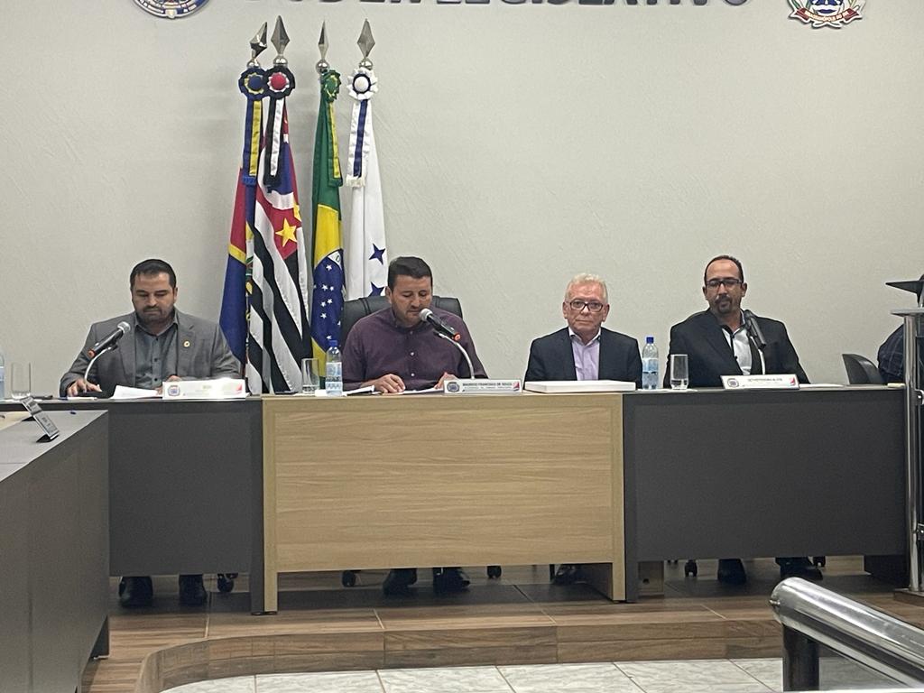 Na imagem aparece o plenário da Câmara Municipal de Sebastianópolis do Sul. O presidente do CRMV-SP compõe a mesa ao lado dos vereadores e o presidente da Casa Legislativa. Atrás deles estão as bandeiras do país, do estado e do município. E eles estão sentados atrás das mesas do plenário.
