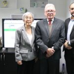 Na foto há dois homens e uma mulher. Eles posam para a foto, olhando e sorrindo para a câmera. Estão em frente a uma televisão em que aparece o site do CRMV-SP, com a sua logomarca.