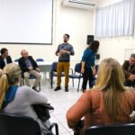 Na foto aparecem pessoas sentadas em carteiras escolares formando uma roda. Ao centro de pé está o secretário de bem-estar animal de Mogi Guaçu. Um homem jovem, moreno, de cabelo curto e óculos de aro preto.