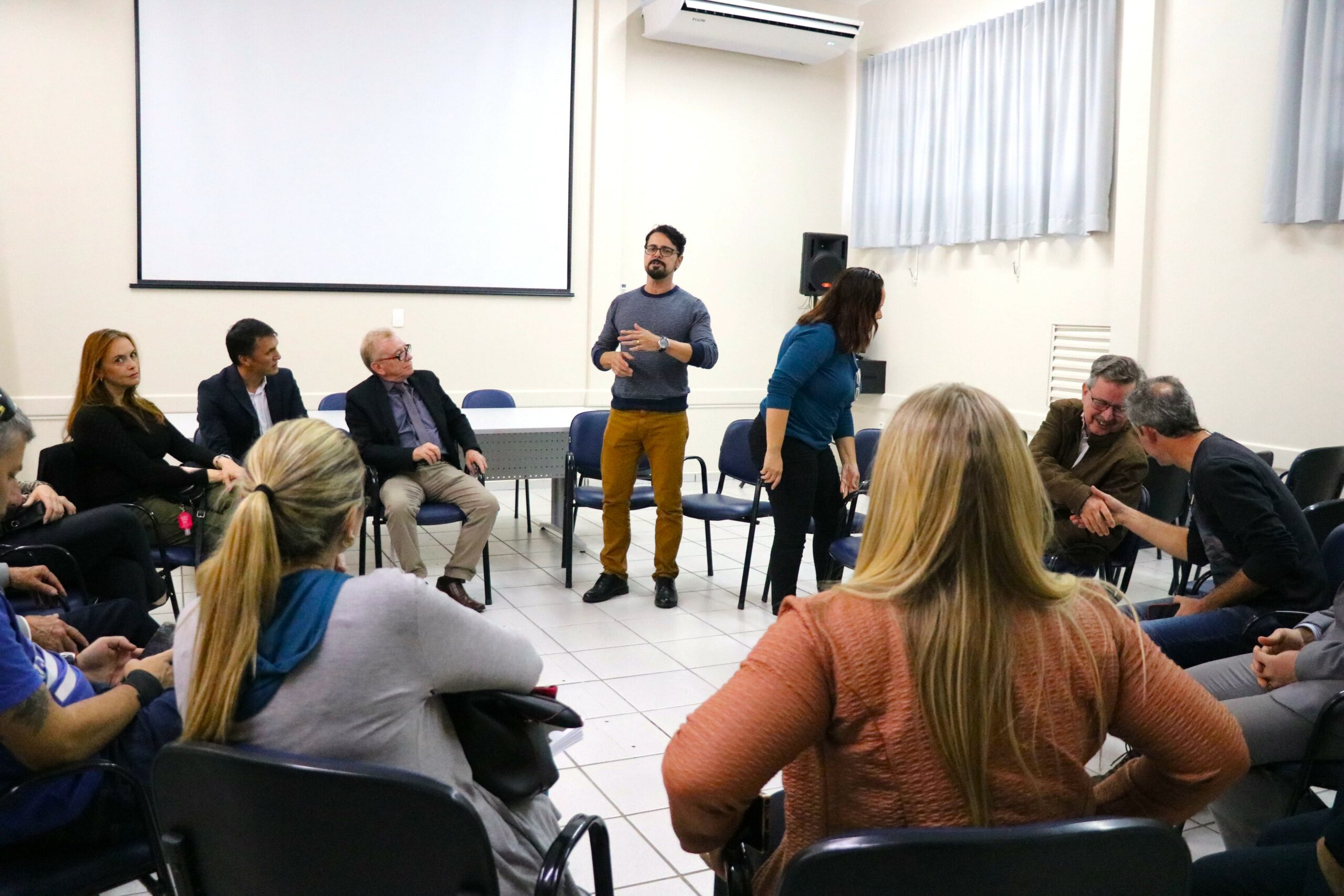 Na foto aparecem pessoas sentadas em carteiras escolares formando uma roda. Ao centro de pé está o secretário de bem-estar animal de Mogi Guaçu. Um homem jovem, moreno, de cabelo curto e óculos de aro preto.