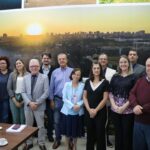 Na foto estão todos os representantes da prefeitura de Araçatuba e do CRMV-SP de pé, posados lado a lado, e sorrindo para a foto em frente a um painel de fotos da cidade. Em destaque nesse painel está a imagem de um por do sol com vista aérea do município.