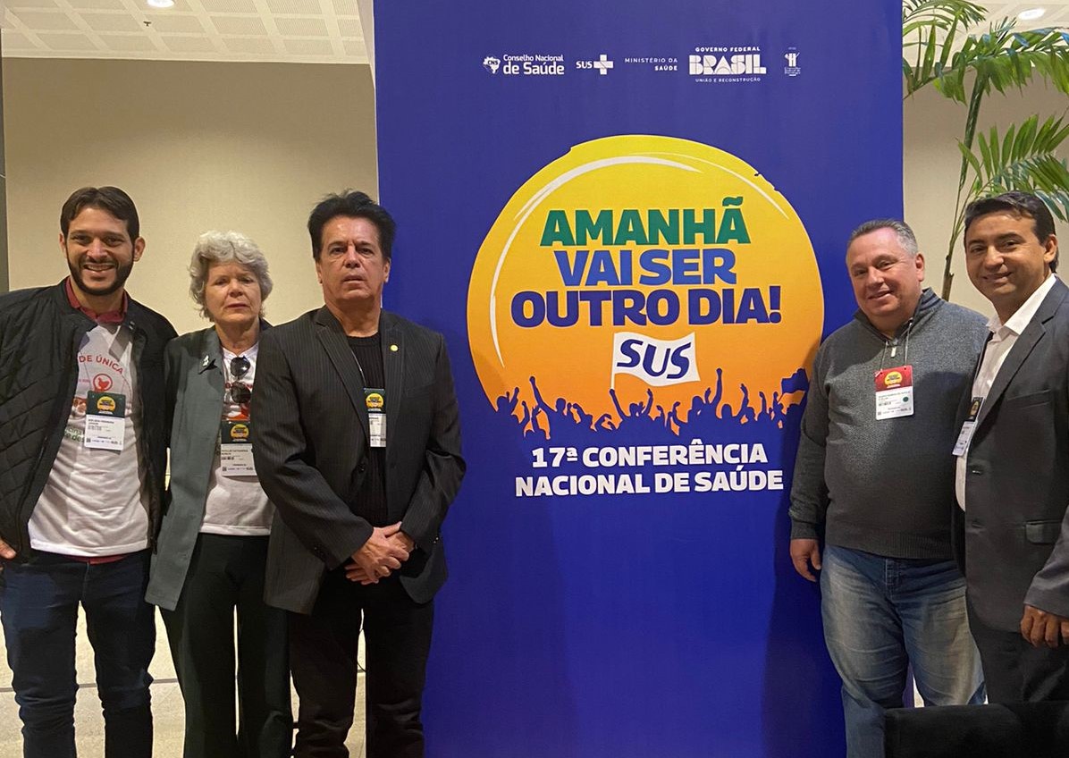 Na imagem há três pessoas, entre elas apenas uma mulher. Eles posam ao lado de um painel da 17ª Conferência Nacional de Saúde, com os dizeres "Amanhã vai ser outro dia!". Eles são médicos-veterinários do CFMV e do CRMV-SP.