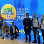 Na foto há seis pessoas em pé, sendo quatro homens e duas mulheres e dois homens agachados, todos posando para a foto.