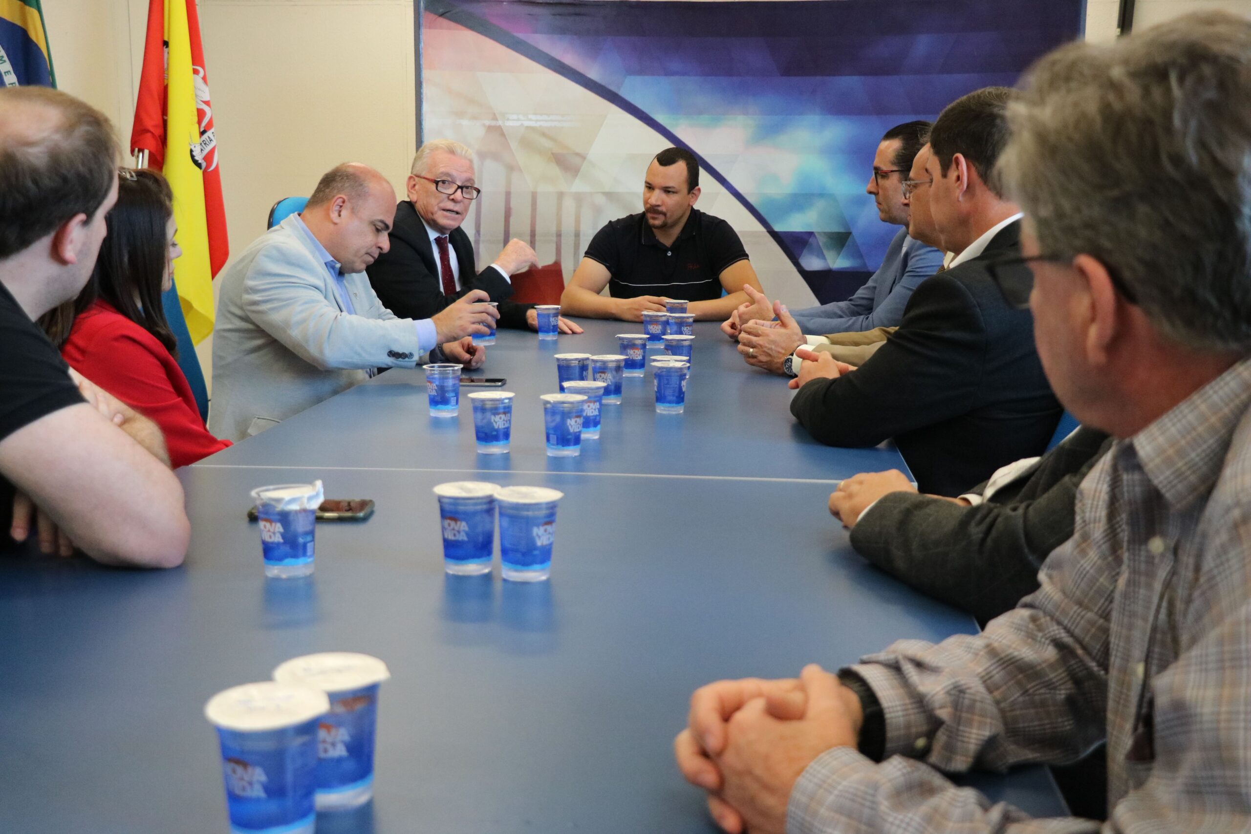 Na foto, aparecem dez pessoas sentadas ao entorno de uma mesa retangular azul. São os representantes do CRMV-SP e na cabeceira, o vereador Dylan Dantas. Ao fundo, a bandeira de Sorocaba.