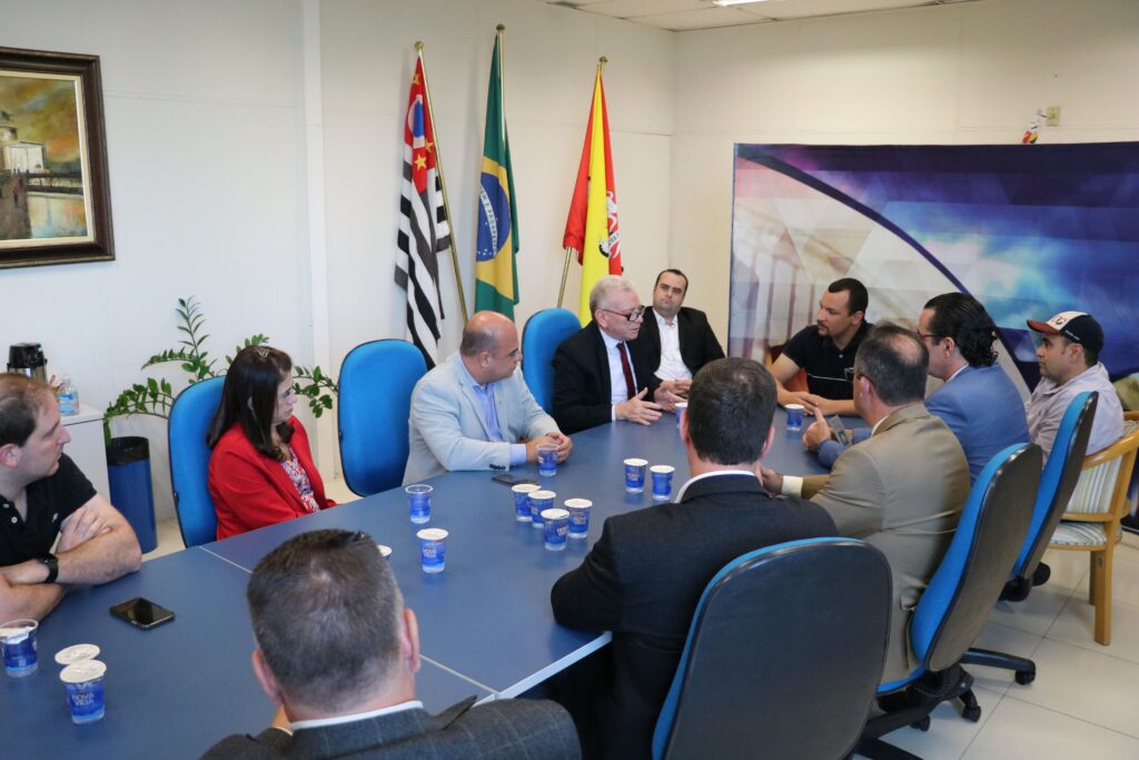 Na foto aparecem onze pessoas sentadas ao entorno de uma retangular azul. São os representantes do CRMV-SP, o vereador Dylan Dantas, o ex-secretário de Meio Ambiente e o assessor Edson Prieto. Eles conversam entre si e o presidente do CRMV-SP gesticula com as mãos ao falar. Ao fundo aparecem as bandeiras de São Paulo, do Brasil e de Sorocaba.