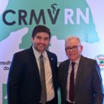 Na foto, o recém-eleito presidente do CRMV-RN está ao lado do presidente do CRMV-SP. Ambos estão sorrindo. Ao fundo, está o cartaz com o logotipo do CRMV-RN, em cor verde.