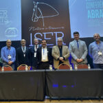 Imagem mostra participantes da Conferência Anual da Associação Brasileira de Veterinários de Equídeos em pé, no palco,