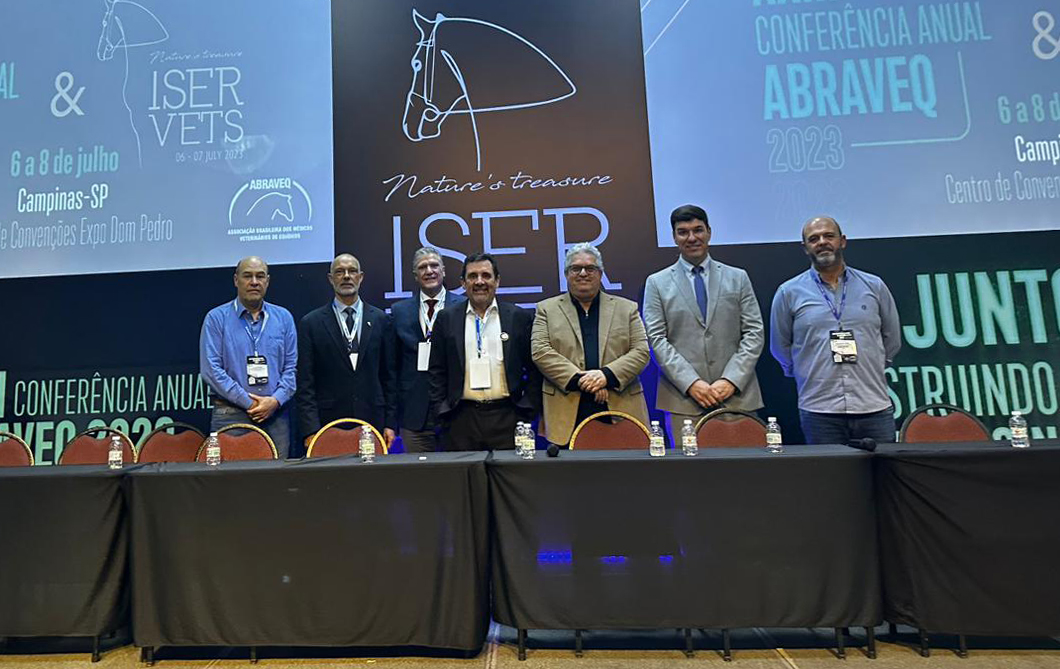 Imagem mostra participantes da Conferência Anual da Associação Brasileira de Veterinários de Equídeos em pé, no palco,