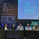 Os participantes da Conferência Anual da Associação Brasileira de Veterinários de Equídeos estão no palco, sentados, e o representante do CRMV-SP, Paulo Corte Neto, está falando ao microfone.