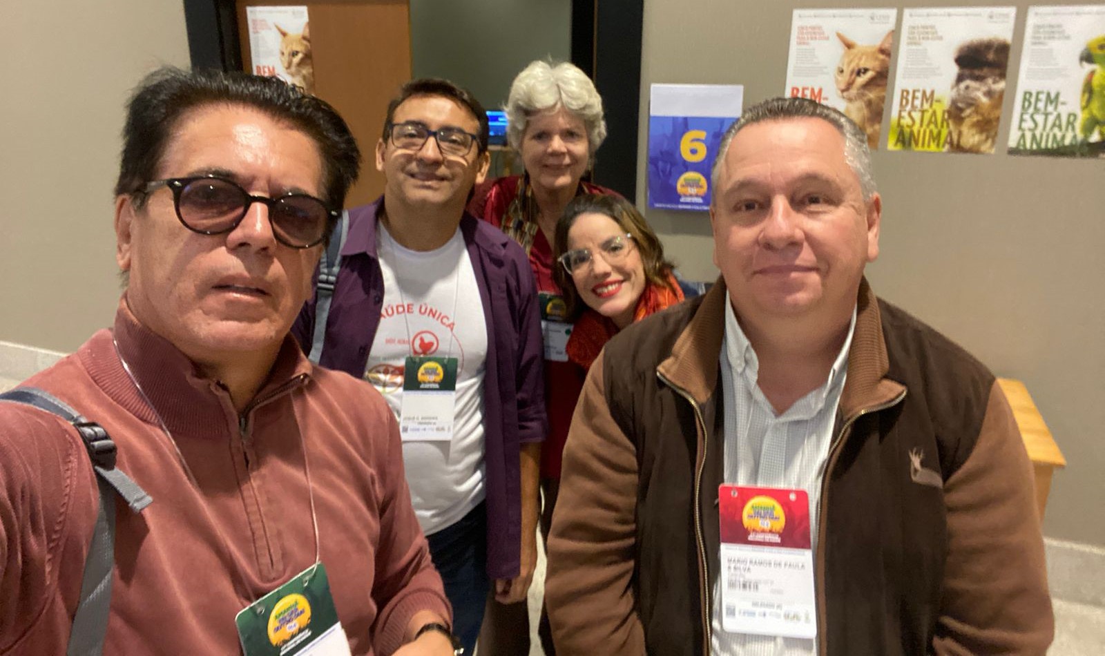 Na foto há cinco pessoas, sendo três homens e duas mulheres. Estão em pé posando para a foto.