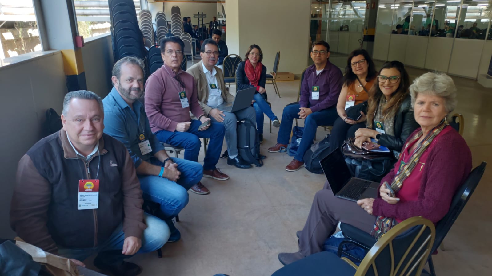 Na foto há nove pessoas, sendo cinco homens e quatro mulheres. Estão sentados em semicírculo posando para a foto.