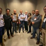 Na foto há nove pessoas, sendo duas mulheres e sete homens. Estão em pé, em um semicírculo, posando para a foto. Estes são os membros da organização do evento ao lado de representantes da CNSPV/CFMV e de delegados durante a 17ª Conferência Nacional de Saúde.