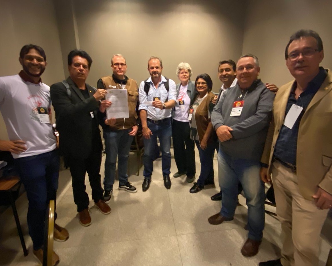 Na foto há nove pessoas, sendo duas mulheres e sete homens. Estão em pé, em um semicírculo, posando para a foto. Estes são os membros da organização do evento ao lado de representantes da CNSPV/CFMV e de delegados durante a 17ª Conferência Nacional de Saúde.