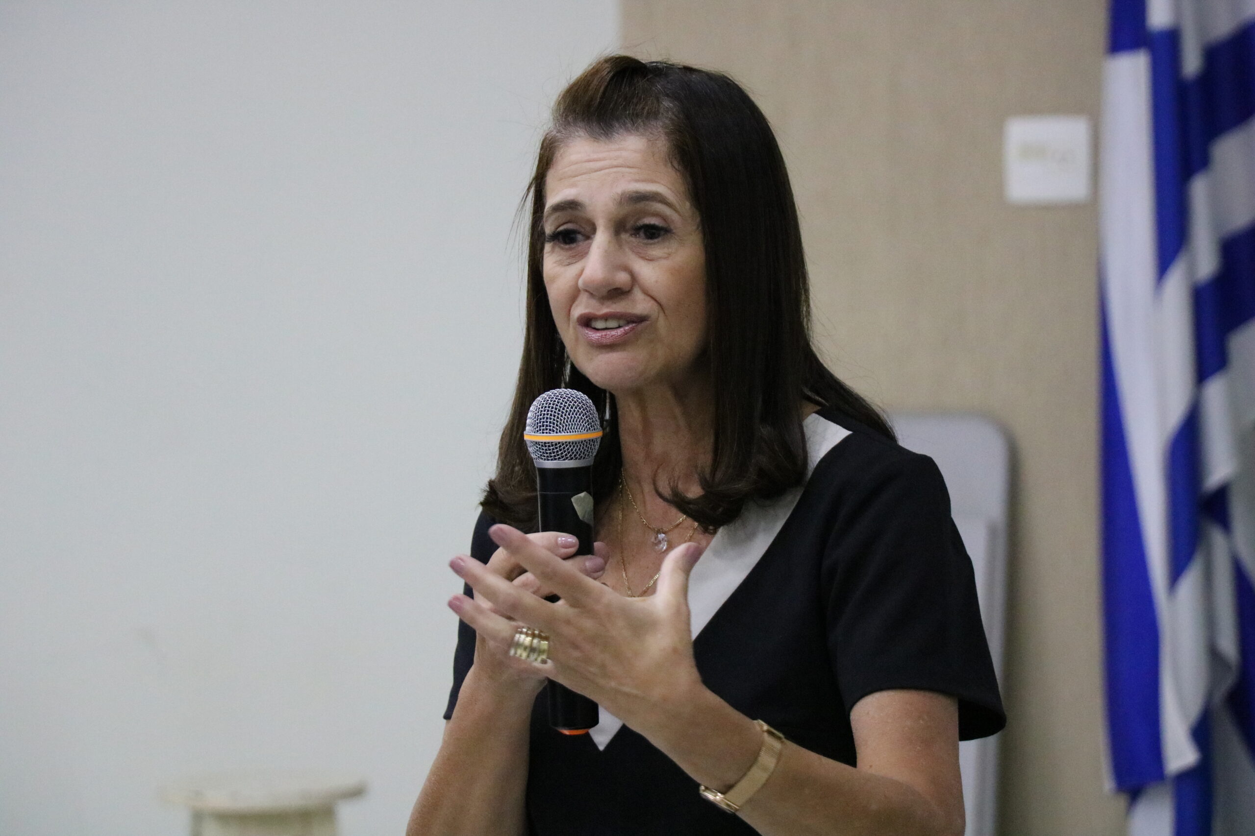 Na imagem aparece em destaque a tesoureira do CRMV-SP. Ela gesticula e fala ao microfone. Ela tem cabelos castanhos alinhados na altura do ombro e veste um macacão de cor preta e detalhe da gola em branco.