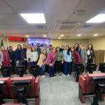 Na foto há 19 pessoas. Elas estão de pé, posicionadas na parte da frente de um auditório com cadeiras estofadas vermelhas. São os participantes do I Encontro Nacional de Perícia Médica-veterinária e Direito. Atrás deles há um telão, um relógio digital com números vermelhos, e as bandeiras do estado de São Paulo e do Brasil. Na foto há duas integrantes da Comissão de Medicina Veterinária do CRMV-SP.