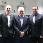 Na foto há três homens de meia idade, sorrindo para a foto, de pé e posados lado a lado. Eles vestem terno cinza com camisa, dois deles usam óculos e outro usa gravata de cor clara. Trata-se dos presidentes do Sindimvet e do CRMV-SP, e do secretário geral da autarquia.