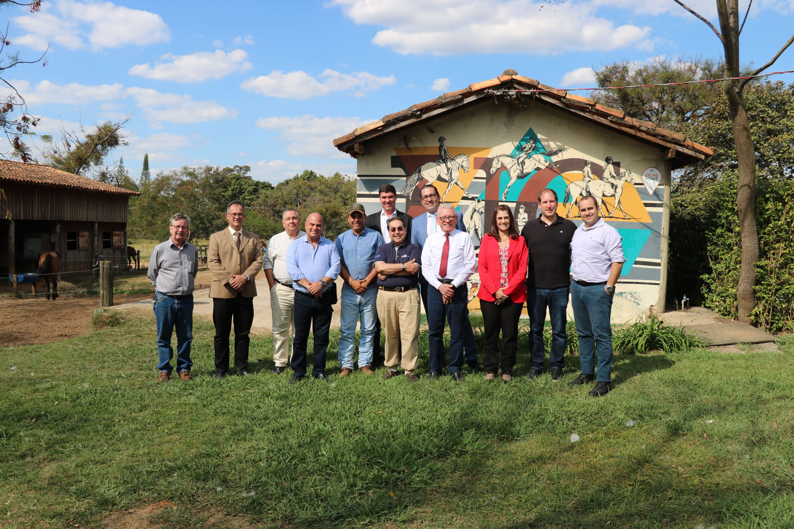 O médico-veterinário Aluísio Marins, diretor técnico da instituição, e o professor e empresário, Luiz Marins, estão na foto posando ao lado dos membros do CRMV-SP. O chão é um gramado bem verde e ao fundo há uma casa. O céu está bem azul e com muitas nuvens brancas.