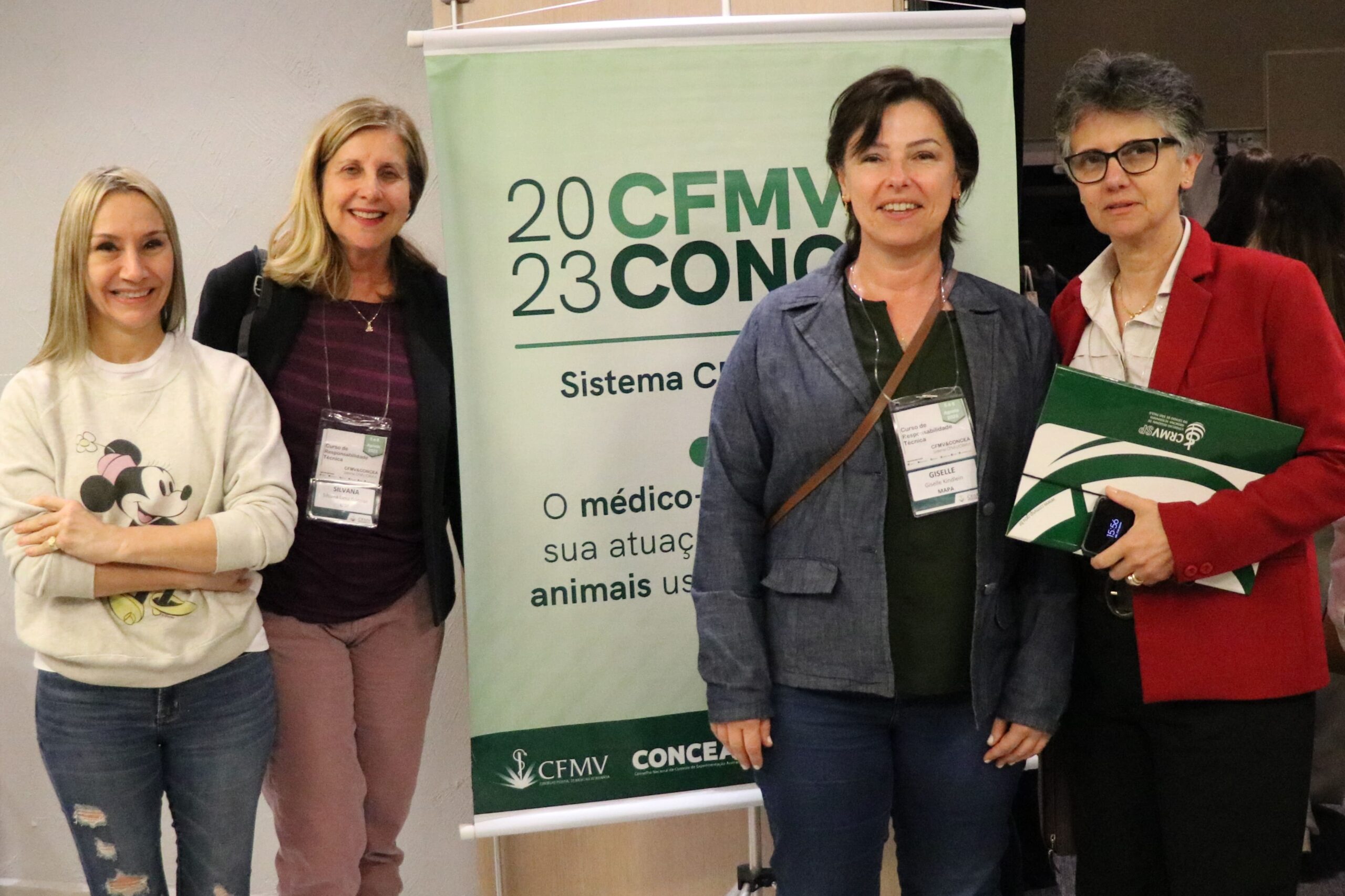 Imagem mostra as quatro mulheres integrantes da Comissão de Pesquisa Clínica do CRMV-SP. Elas posam ao lado do banner do evento. Estão de pé e sorriem para a foto.