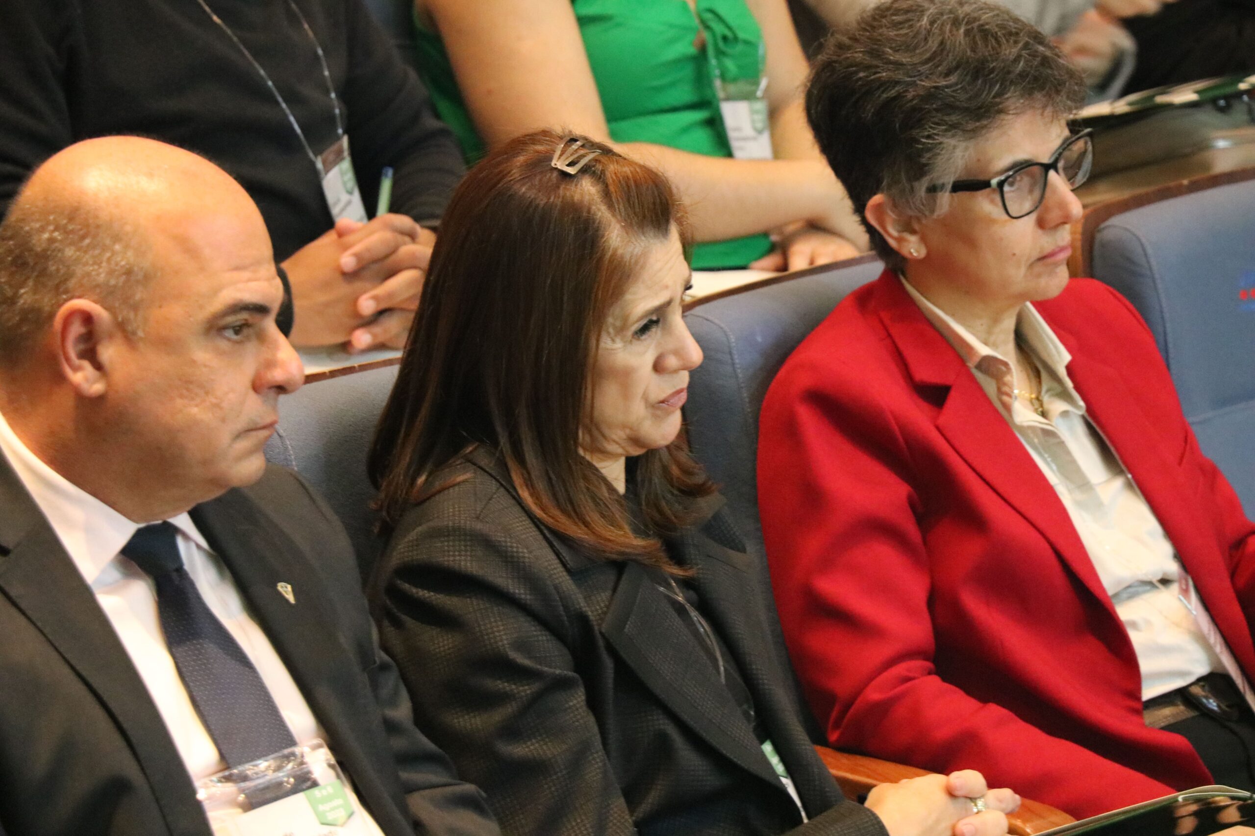 Imagem foca em três pessoas sentadas no auditório. Duas mulheres e um homem. Trata-se do vice-presidente e a tesoureira do CRMV-SP, e a presidente da Comissão Técnica de Pesquisa Clínica. Eles estão atentos a palestra e aparecem de perfil.