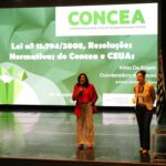 Na imagem aparecem as palestrantes Luisa Maria e Kátia De Angelis em cima do palco e a frente da projeto de um slide sobre as legislações do Concea.