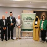 Na imagem aparecem cinco homens e duas mulheres posando ao lado do banner do evento do Concea e do CFMV. Uma das mulheres utiliza véu cobrindo cabelos e rosto. Trata-se da diretoria do CRMV-SP, do presidente do CFMV, do sheikh e sua esposa.