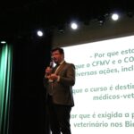 Na imagem aparece o diretor do departamento jurídico do CFMV ao palco, falando ao microfone. Ao fundo um slide sobre a legislação do CFMV.