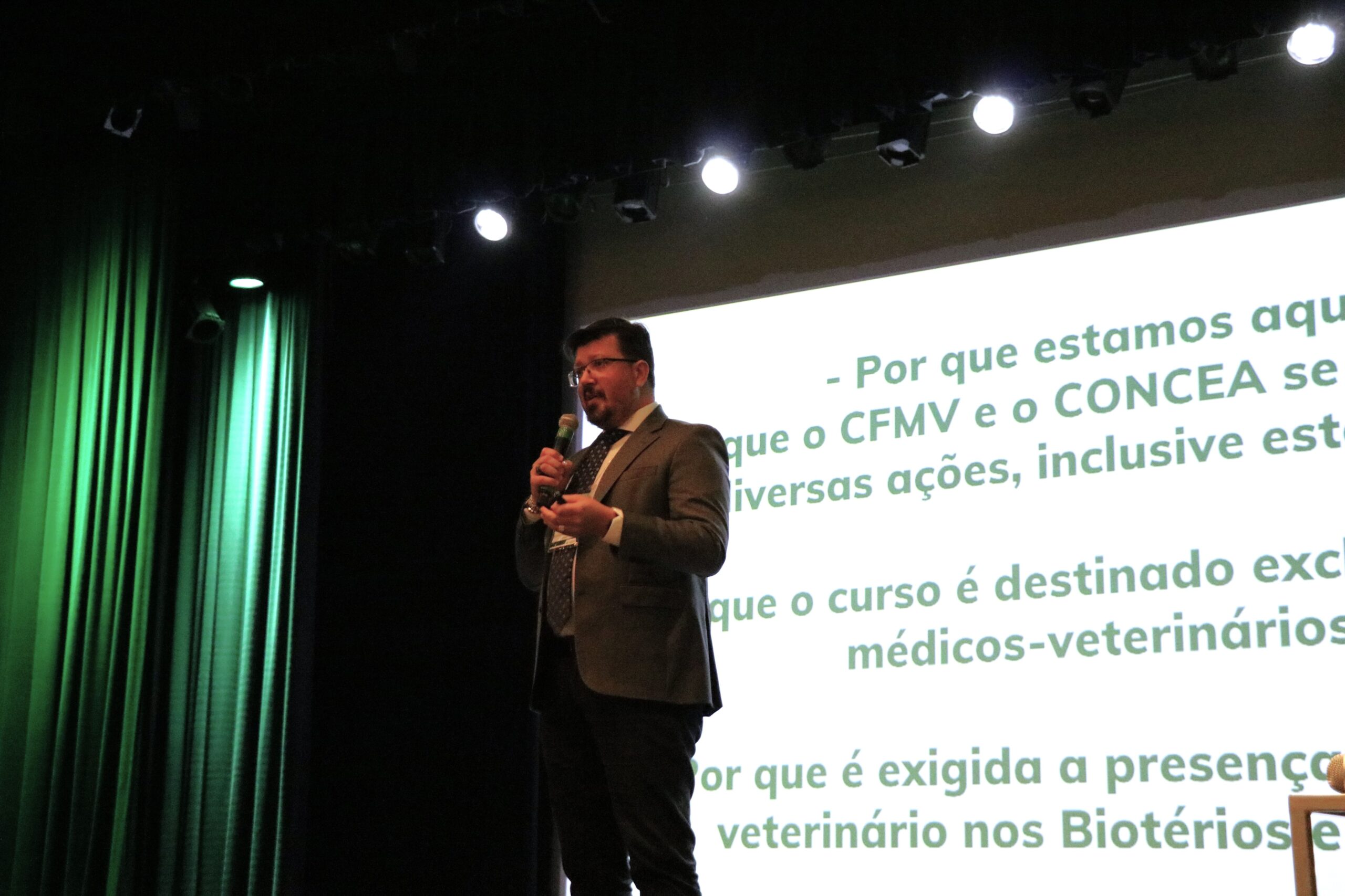 Na imagem aparece o diretor do departamento jurídico do CFMV ao palco, falando ao microfone. Ao fundo um slide sobre a legislação do CFMV.