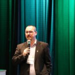 A imagem traz o assessor técnico do CRMV-SC falando ao microne. Atrás uma cortina com iluminação na cor verde.