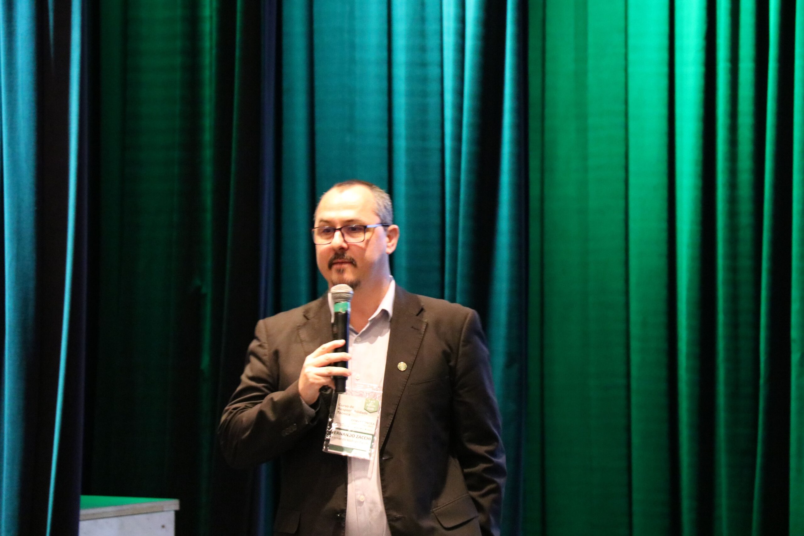 A imagem traz o assessor técnico do CRMV-SC falando ao microne. Atrás uma cortina com iluminação na cor verde.