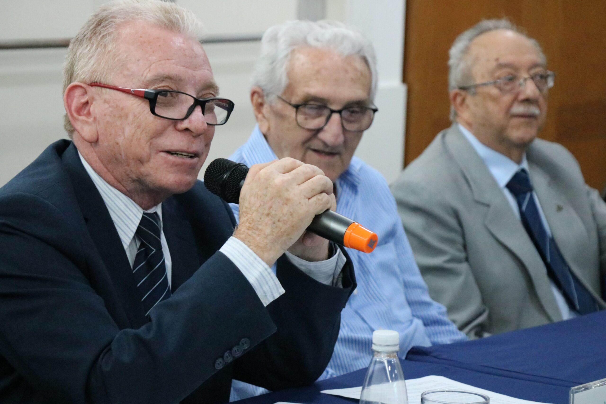 Na foto aparecem três homens sentados atrás de uma mesa com toalha azul. Em destaque está o presidente do CRMV-SP, que fala ao microfone, e em segundo plano está o presidente do CFMV e o representante regional de Campinas.