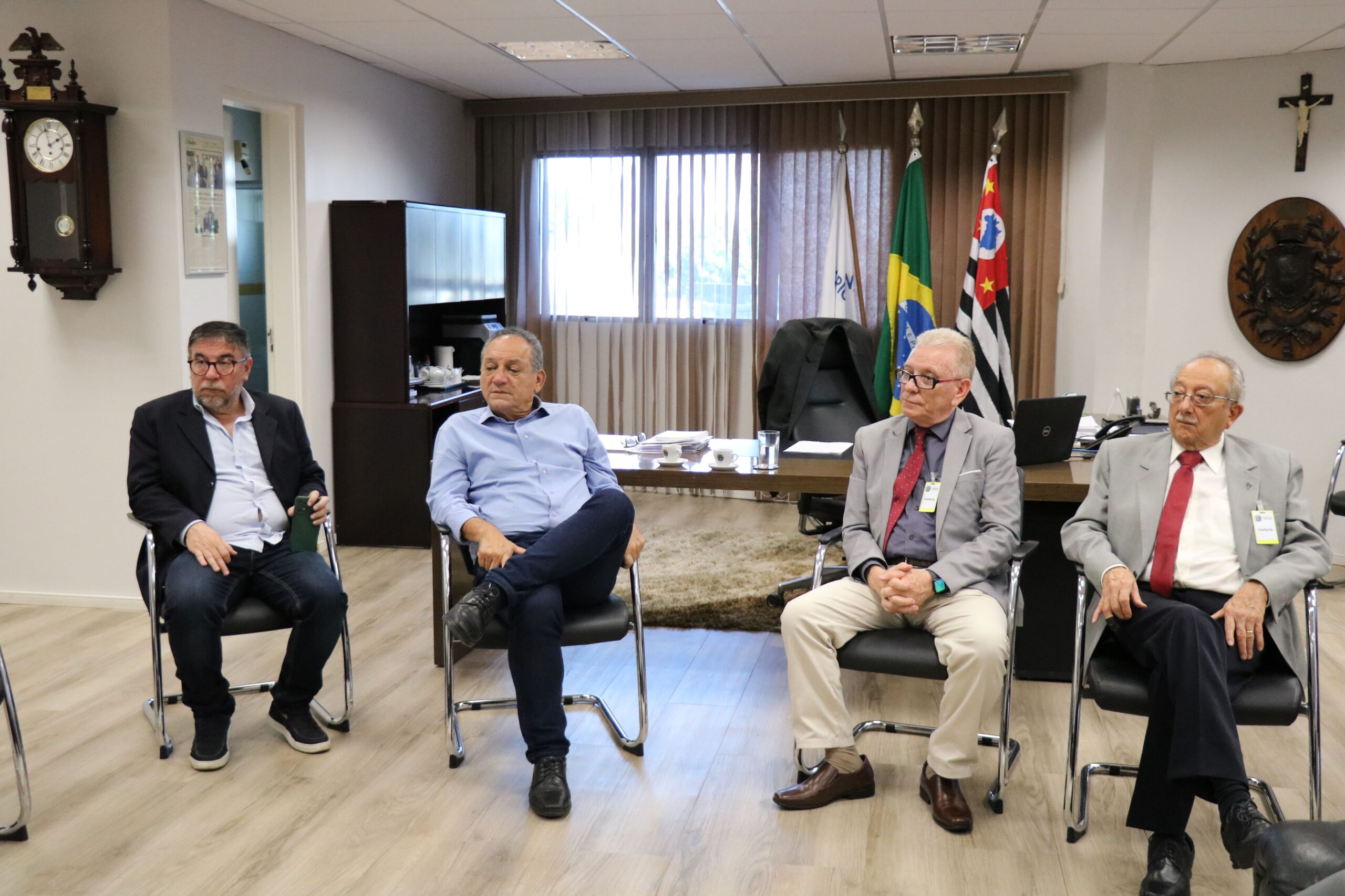 Na foto aparecem quatro homens com roupas sociais sentados em cadeiras em uma sala ampla com as bandeiras do Brasil, do estado de São Paulo e do município de Campinas. Trata-se do presidente da Câmara Municipal de Campinas e de seu assessor, além do presidente do CRMV-SP e do representante regional. Eles estão no gabinete do vereador.