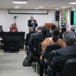 A foto mostra a platéia e um homem apresentando a palestra.