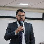 A foto mostra um homem ao microfone.