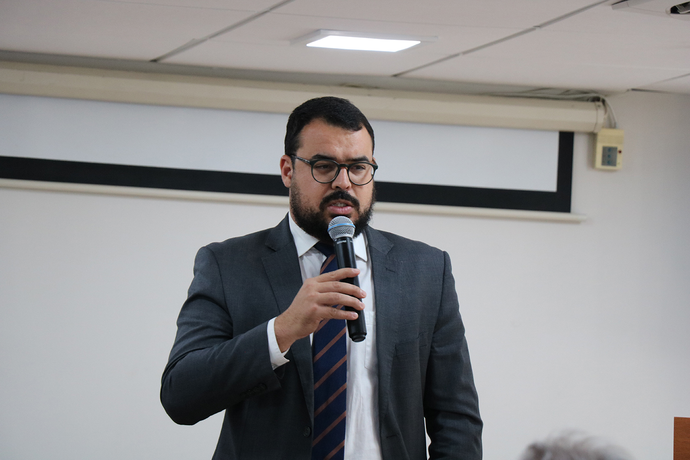 A foto mostra um homem ao microfone.