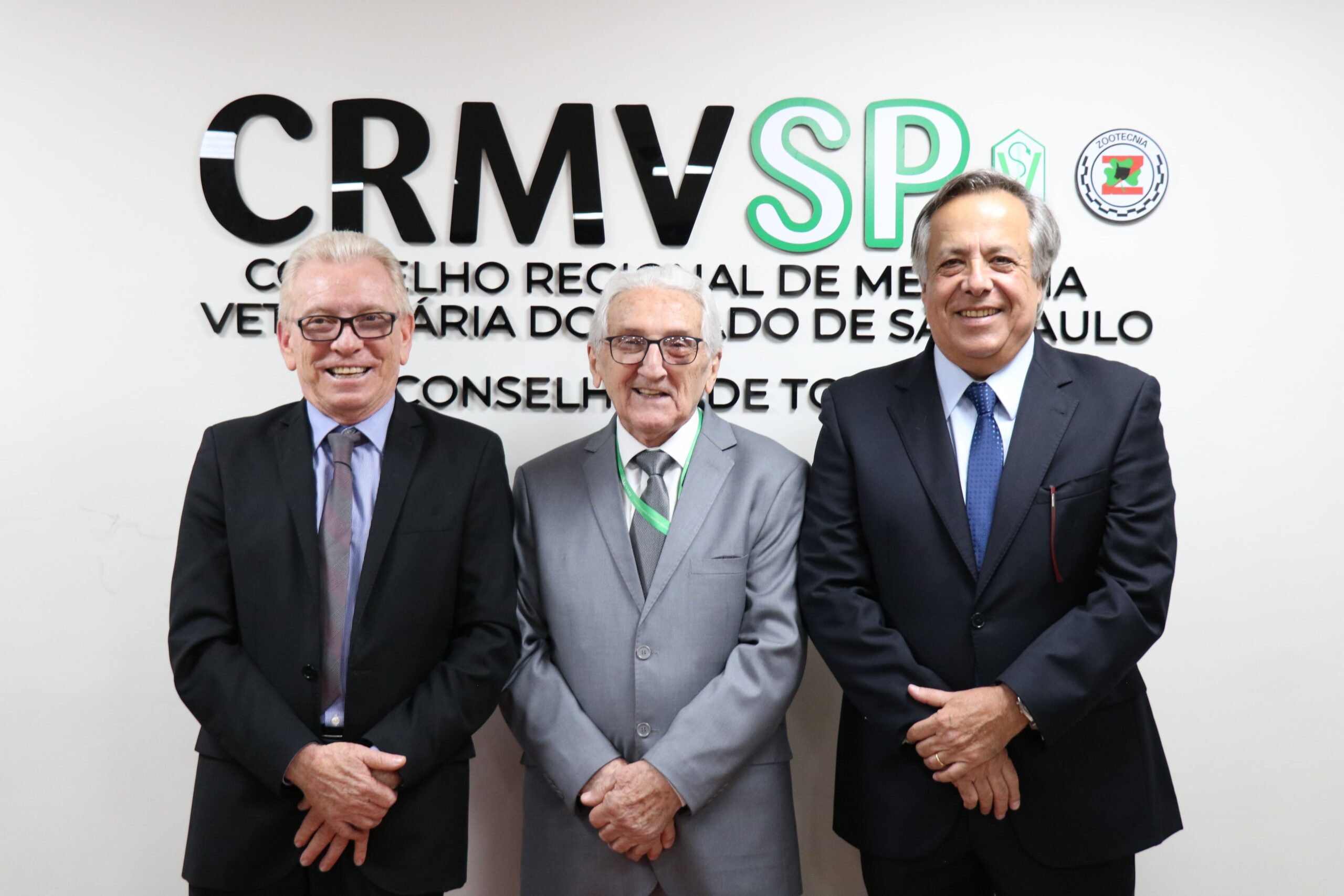 O presidente atual e os presidentes anteriores do CRMV-SP, Odemilson Donizete Mossero, Francisco Cavalcanti de Almeida e Mário Eduardo Pulga, posam em frente ao logotipo do Regional, que são letras na parede com o nome do Conselho e os símbolos da Medicina Veterinária e da Zootecnia.