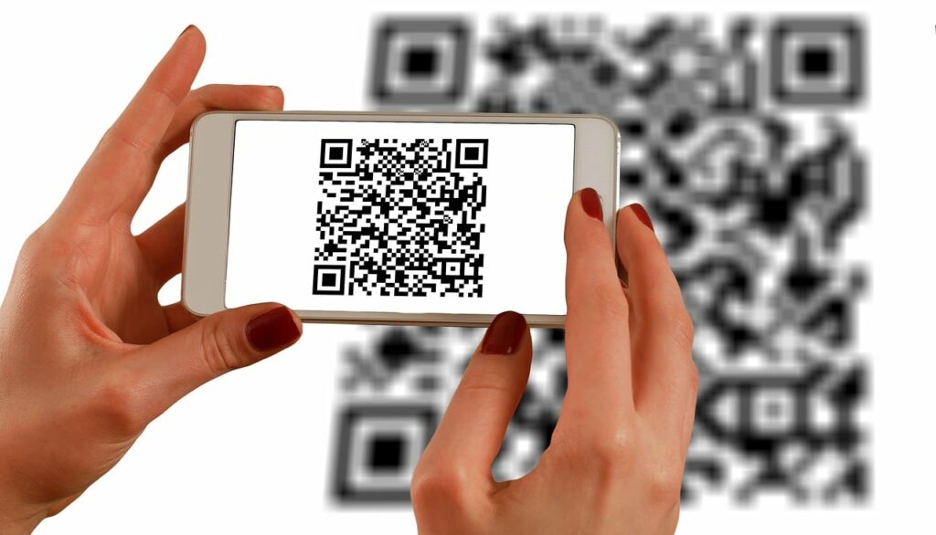 A imagem mostra uma mão que está segurando um celular, registrando um QR Code.