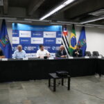 A imagem traz representantes do CRMV-SP ao lado de representantes da Prefeitura de Ribeirão Preto. São sete pessoas, sentadas à mesa, sendo seis homens e uma mulher. Atrás deles aparecem bandeiras do Brasil, do estado de São Paulo e do município e um painel azul e branco com o logotipo da Prefeitura.