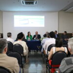 A imagem traz os representantes do CRMV-SP, sentados à mesa, ao fundo, e a plateia, de costas. O vice-presidente, de terno escuro, fala ao microfone.