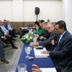 A imagem mostra os seis representantes do CRMV-SP, uma mulher de blazer verde, e cinco homens de terno escuro, sentados à mesa, sendo observados pelas pessoas presentes ao evento.
