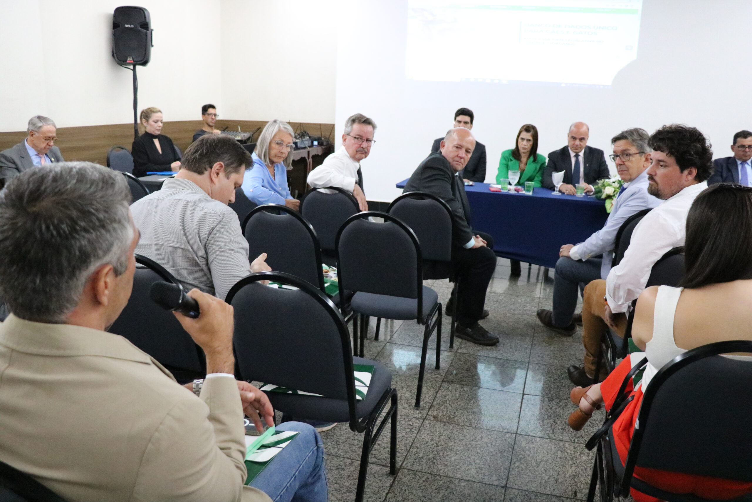 A imagem traz um homem com o microfone na mão fazendo uma pergunta e sendo observado pelos representantes do CRMV-SP que estão à mesa e pelos demais participantes do evento.
