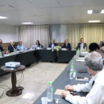 A imagem traz uma mesa em formato de U, com representantes do CRMV-SP, homens e mulheres, de roupa social. O presidente do Conselho, de óculos, fala ao microfone na abertura da Sessão Plenária.