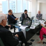Na foto, estão sentados e conversam os participantes da reunião do PRODES: o presidente do CRMV-SP, Odemilson Donizete Mossero (primeiro ao fundo); o conselheiro do CFMV, Paulo Araújo de Guerra (à direita); a vice-presidente do CFMV, Ana Elisa de Souza Almeida; o conselheiro do CFMV, Marcílio Magalhães Vaz de Oliveira (primeiro, à frente); o presidente do CRMV-BA, Altair Santana de Oliveira (primeiro, à direita); o assessor administrativo, chefe do Núcleo de Apoio aos Regionais (NAR) do CFMV, Igor Pinto de Andrade; e a presidente do CRMV-PE, Maria Elisa Araújo.
