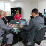 Na foto, estão sentados e conversam os participantes da reunião do PRODES: o presidente do CRMV-SP, Odemilson Donizete Mossero (primeiro ao fundo); o conselheiro do CFMV, Paulo Araújo de Guerra (à direita); a vice-presidente do CFMV, Ana Elisa de Souza Almeida; o conselheiro do CFMV, Marcílio Magalhães Vaz de Oliveira (primeiro, à frente); o presidente do CRMV-BA, Altair Santana de Oliveira (primeiro, à direita); o assessor administrativo, chefe do Núcleo de Apoio aos Regionais (NAR) do CFMV, Igor Pinto de Andrade; e a presidente do CRMV-PE, Maria Elisa Araújo.