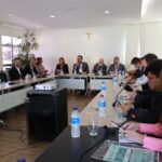 A foto mostra os participantes, sentados durante o evento.