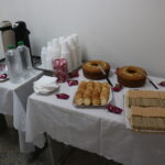 Na foto, mesa decorada com bolo, bolachas, bombons, café, água.