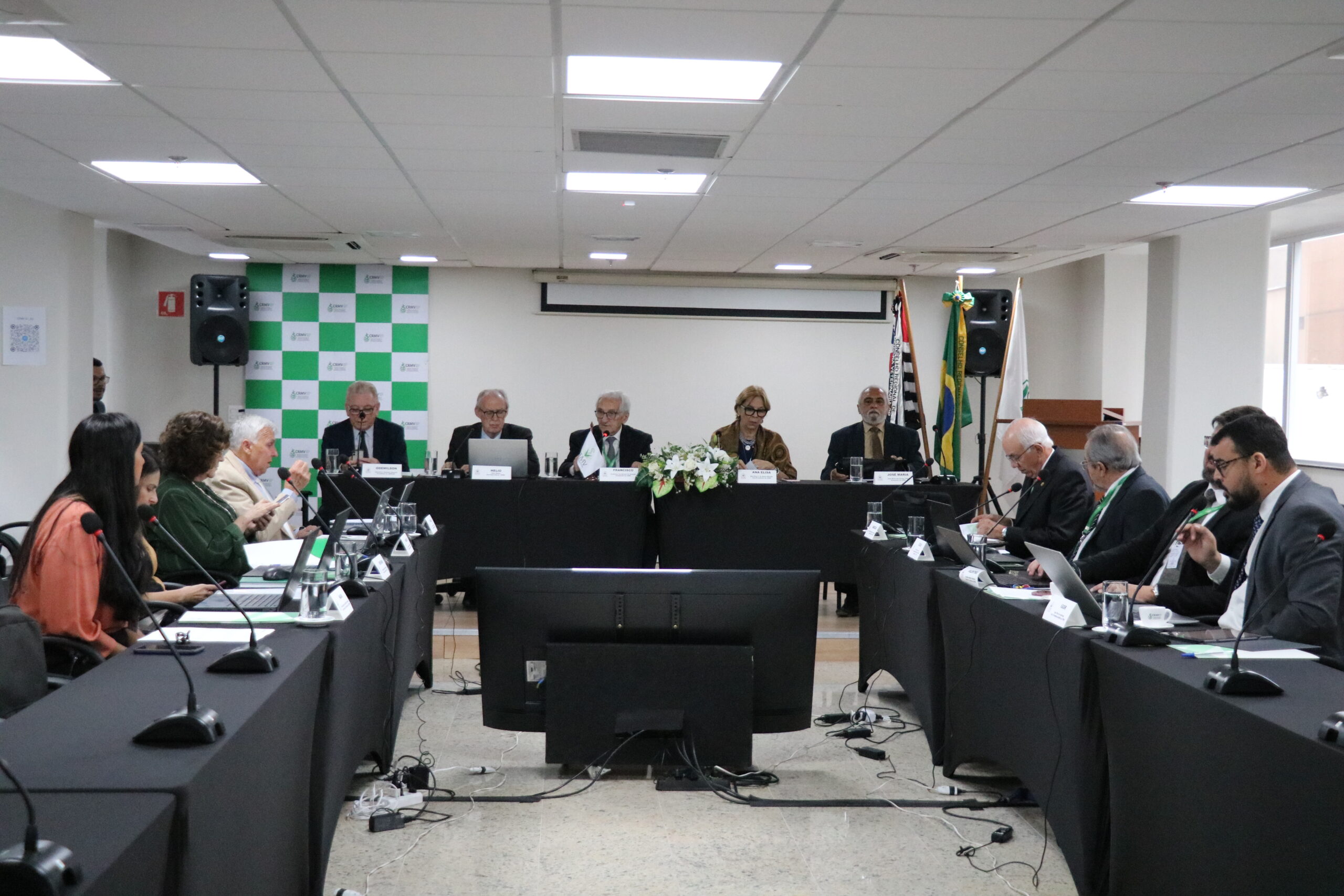 Na foto, membros do plenário estão sentados na sala, em disposição de quadrado.